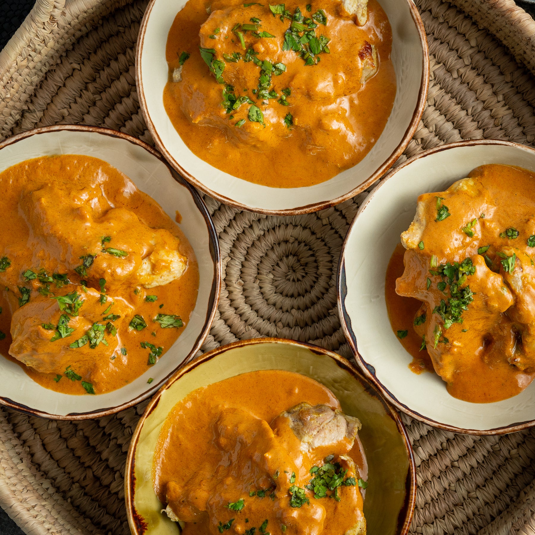 4 dishes of butter chicken curry sprinkled with herbss